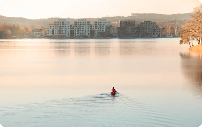 En vacker vy av en sjö intill en stadsdel. En person är ute och paddlar i en kanot i sjön.