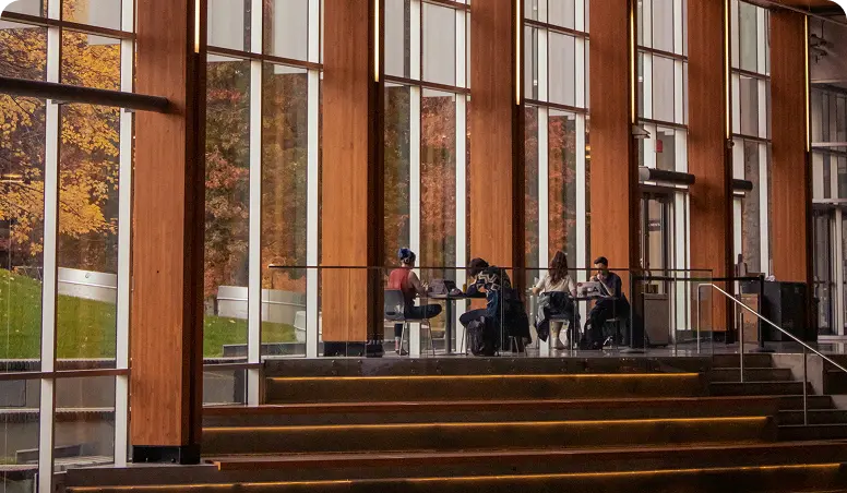 På bilden ser vi människor som sitter och arbetar vid bord inuti en kontorsbyggnad